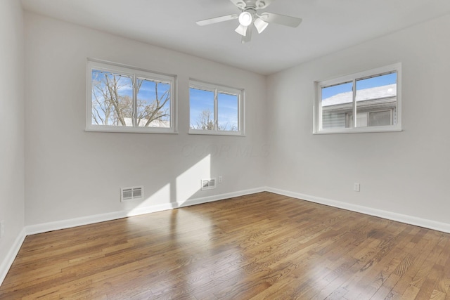 unfurnished room with a ceiling fan, visible vents, baseboards, and wood finished floors