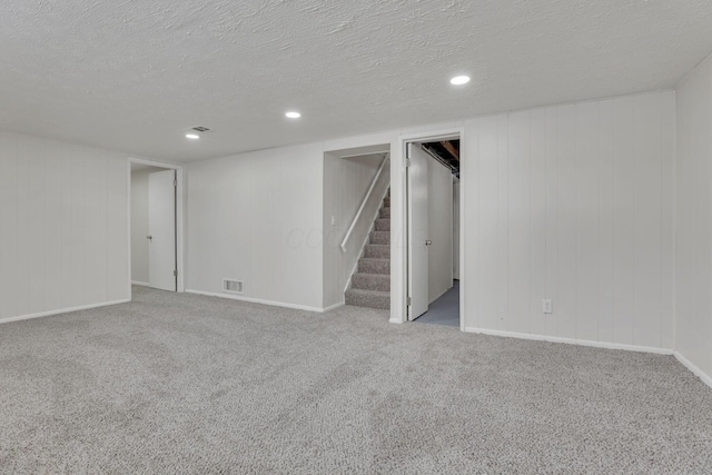 finished below grade area with light carpet, stairs, visible vents, and a textured ceiling