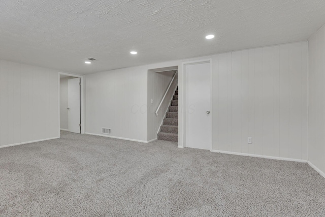 finished below grade area featuring a textured ceiling, carpet floors, stairway, and visible vents