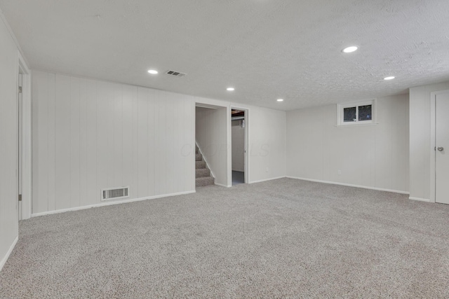 finished below grade area featuring a textured ceiling, carpet floors, stairway, and visible vents