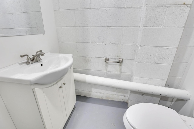 bathroom featuring toilet, concrete floors, vanity, and concrete block wall