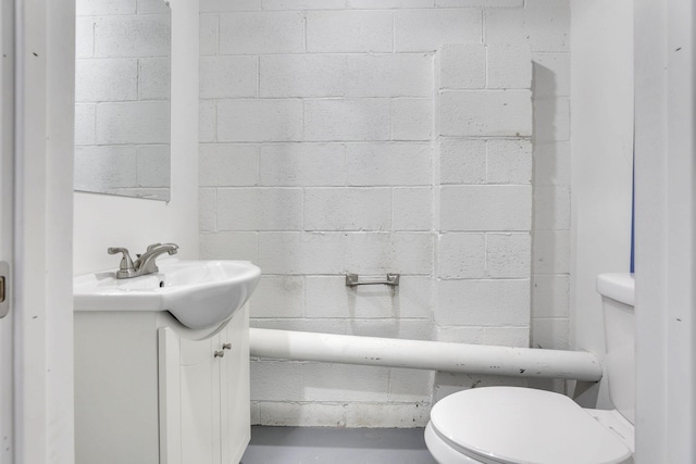 bathroom with concrete block wall, concrete floors, toilet, and vanity