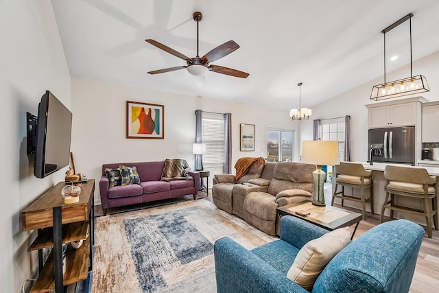 living area featuring vaulted ceiling, ceiling fan with notable chandelier, and light wood-style flooring