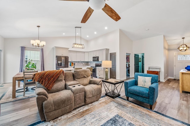 living room featuring light wood finished floors, baseboards, ceiling fan with notable chandelier, high vaulted ceiling, and recessed lighting