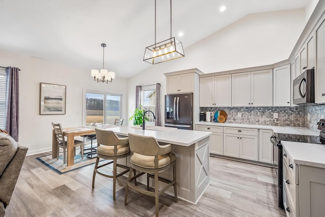 kitchen featuring a center island with sink, light countertops, hanging light fixtures, and black appliances