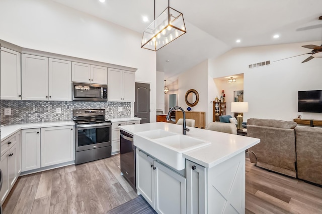 kitchen with a kitchen island with sink, visible vents, open floor plan, light countertops, and appliances with stainless steel finishes