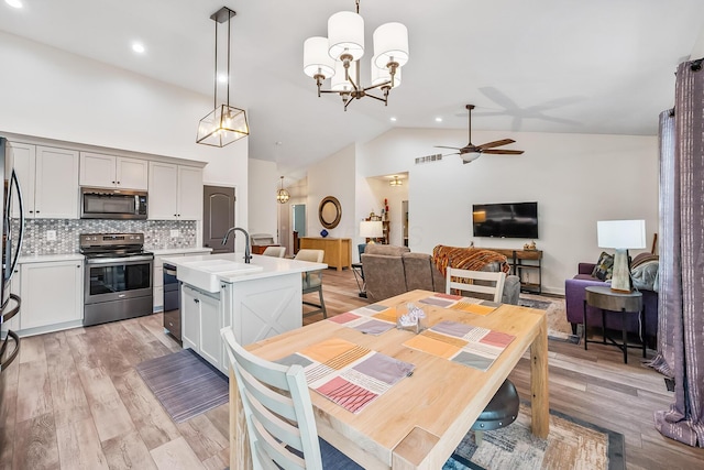 dining space with ceiling fan with notable chandelier, high vaulted ceiling, and light wood finished floors