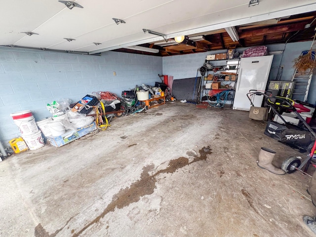 garage with freestanding refrigerator and concrete block wall