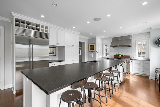 kitchen with dark countertops, a spacious island, wall chimney exhaust hood, and premium appliances