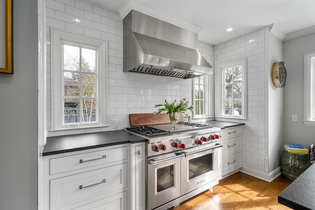 kitchen featuring white cabinetry, double oven range, backsplash, range hood, and dark countertops