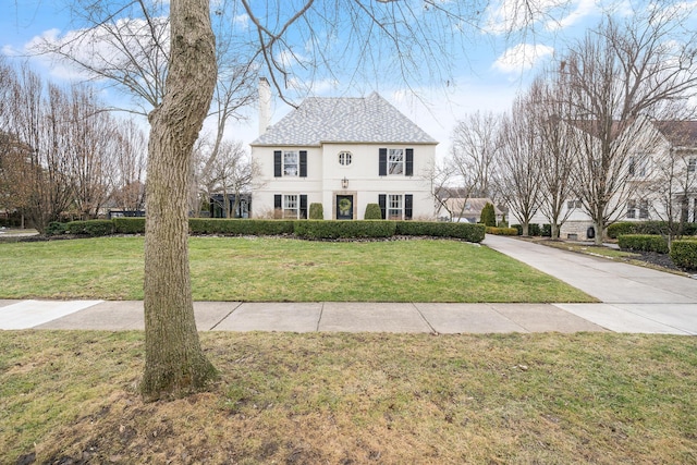 colonial inspired home featuring a front yard, a chimney, and stucco siding