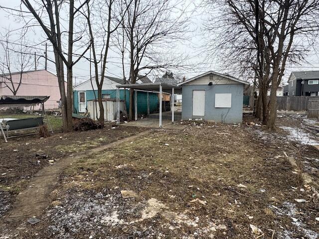 back of property with fence, a carport, and an outbuilding