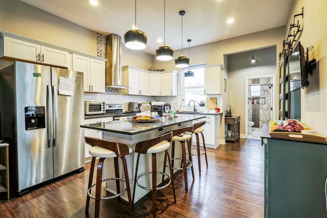 kitchen featuring stainless steel appliances, a sink, a kitchen island, white cabinetry, and wall chimney exhaust hood