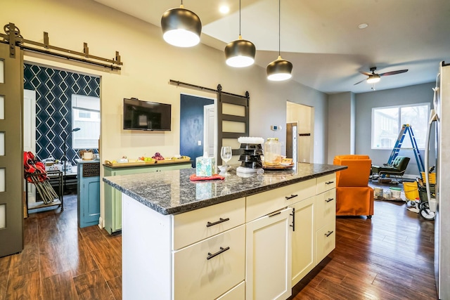 kitchen with a barn door, white cabinets, hanging light fixtures, a center island, and dark stone countertops