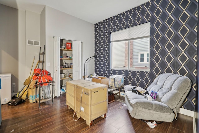 office with an accent wall, dark wood-type flooring, visible vents, baseboards, and wallpapered walls