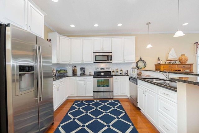 kitchen featuring white cabinets, a peninsula, stainless steel appliances, light wood-style floors, and a sink