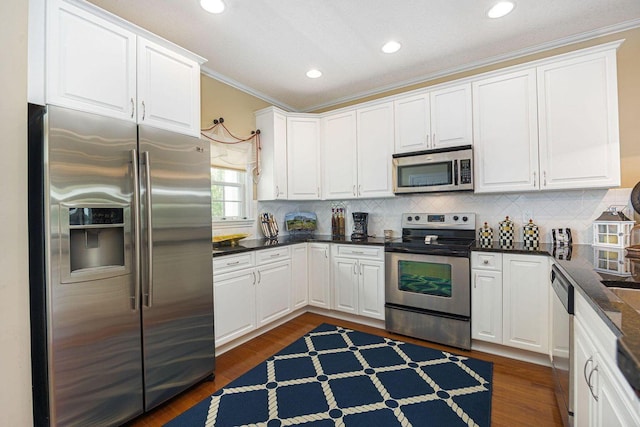 kitchen with white cabinets, ornamental molding, dark wood-style flooring, stainless steel appliances, and backsplash