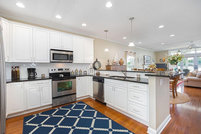 kitchen with stainless steel appliances, a peninsula, wood finished floors, a sink, and open floor plan