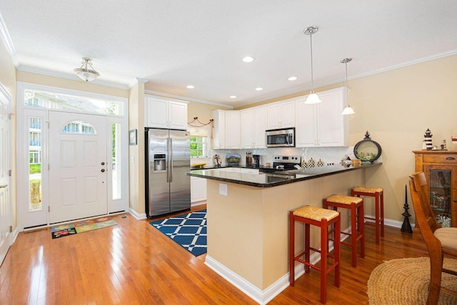 kitchen with white cabinets, light wood-style flooring, a peninsula, stainless steel appliances, and a kitchen bar