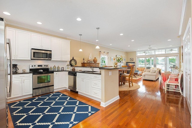 kitchen with stainless steel appliances, a peninsula, wood finished floors, a sink, and dark countertops