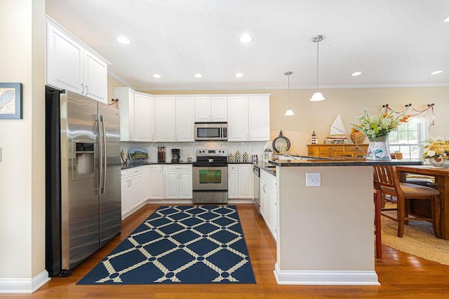 kitchen featuring a peninsula, wood finished floors, white cabinetry, appliances with stainless steel finishes, and dark countertops