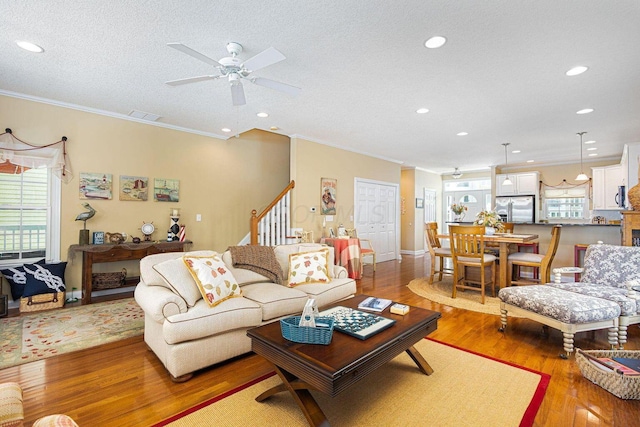 living area with visible vents, a wealth of natural light, ornamental molding, and light wood-style flooring