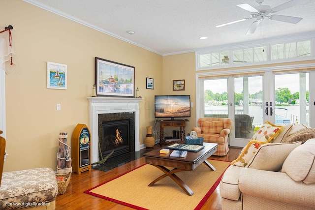 living room featuring french doors, ornamental molding, a fireplace with flush hearth, a textured ceiling, and wood finished floors