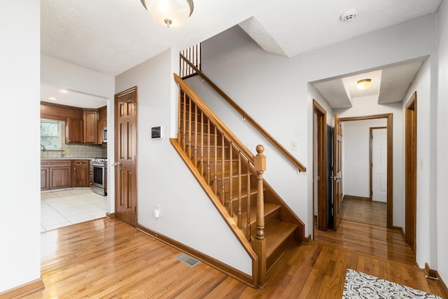 staircase featuring baseboards, a textured ceiling, visible vents, and wood finished floors