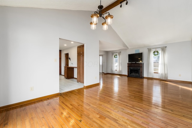 unfurnished living room featuring a fireplace, high vaulted ceiling, light wood finished floors, a chandelier, and baseboards