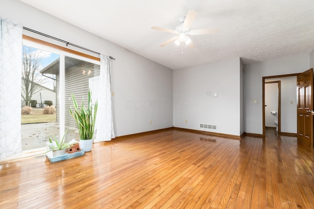 empty room featuring baseboards, visible vents, hardwood / wood-style flooring, ceiling fan, and a textured ceiling