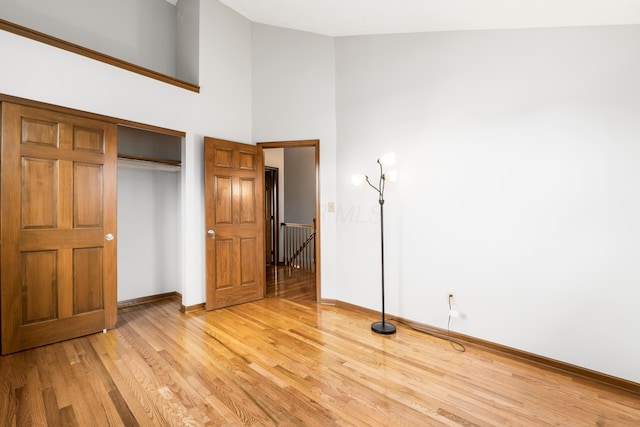 unfurnished bedroom featuring high vaulted ceiling, a closet, light wood-style flooring, and baseboards