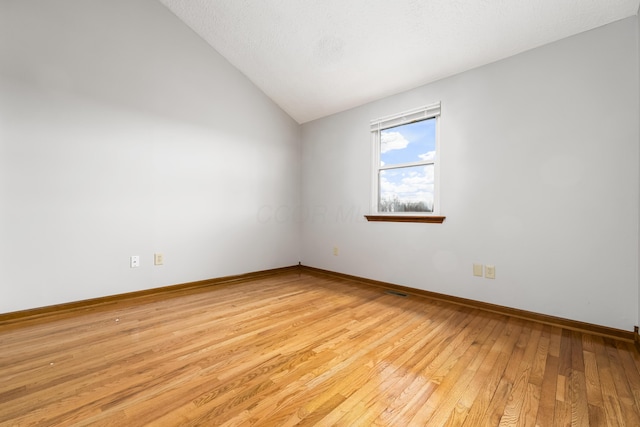 spare room with light wood-type flooring, lofted ceiling, and baseboards