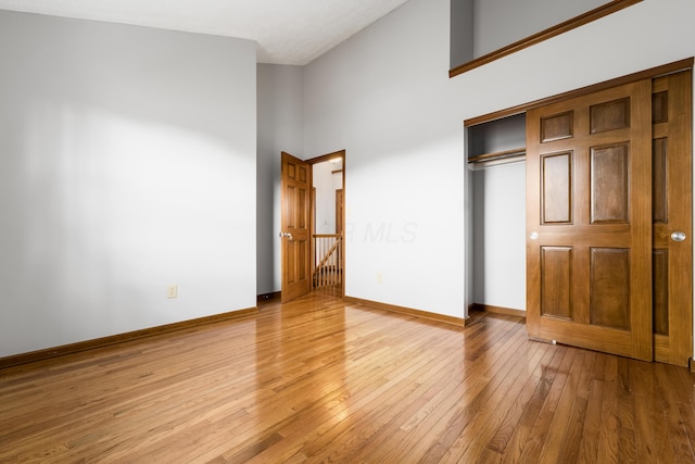 unfurnished bedroom featuring a closet, wood-type flooring, a towering ceiling, and baseboards