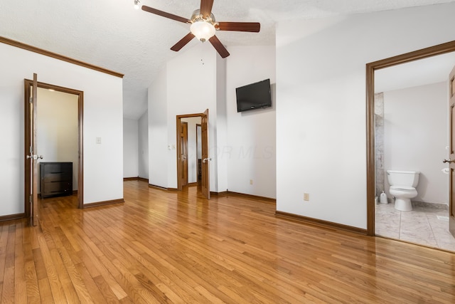 unfurnished bedroom with a textured ceiling, high vaulted ceiling, baseboards, light wood finished floors, and ensuite bath