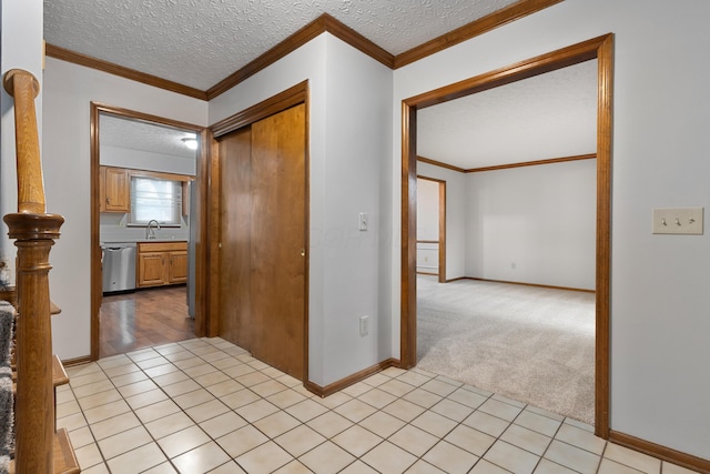 hall with a textured ceiling, light tile patterned floors, light colored carpet, a sink, and ornamental molding