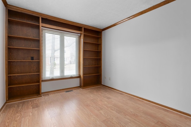 empty room with light wood finished floors, baseboards, visible vents, a textured ceiling, and crown molding