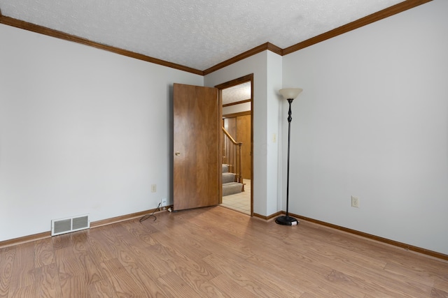 unfurnished room featuring a textured ceiling, wood finished floors, visible vents, ornamental molding, and stairway