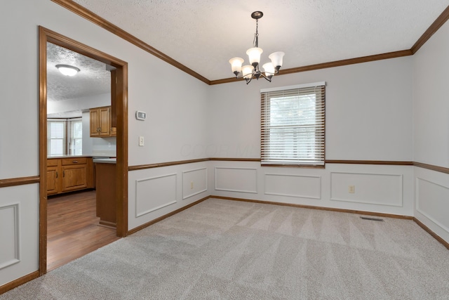 empty room featuring visible vents, light colored carpet, ornamental molding, a textured ceiling, and a chandelier