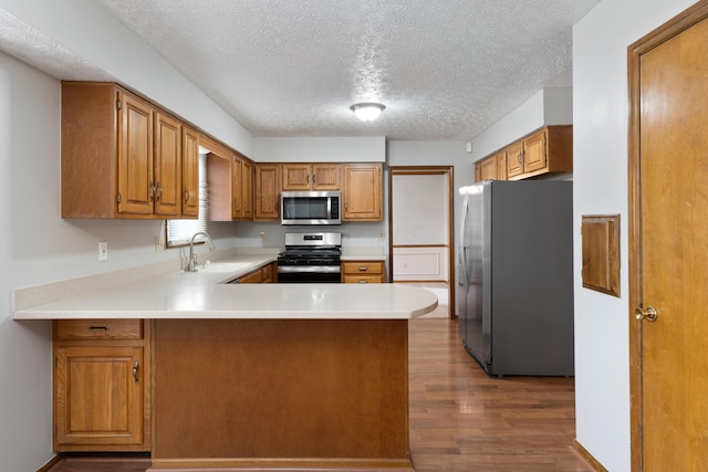 kitchen with stainless steel appliances, dark wood-type flooring, a peninsula, a sink, and light countertops