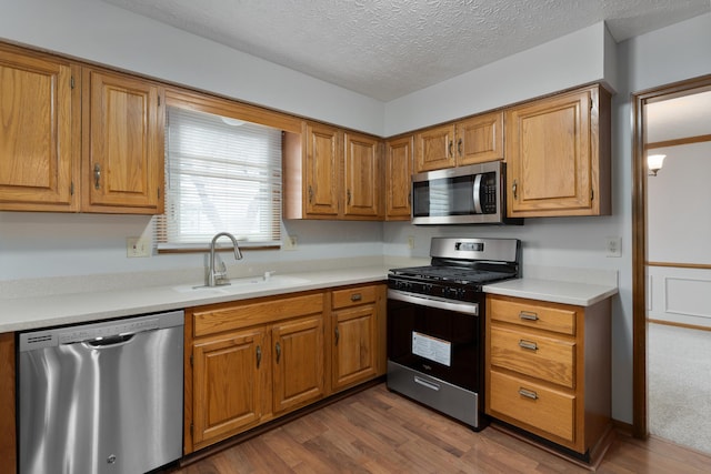 kitchen with stainless steel appliances, dark wood finished floors, a sink, and light countertops