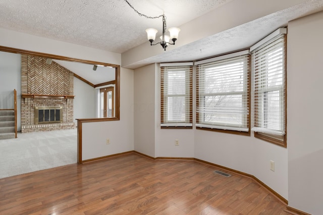 interior space with a chandelier, a textured ceiling, a fireplace, wood finished floors, and visible vents