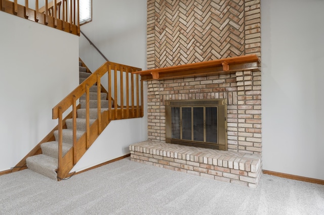 unfurnished living room featuring a brick fireplace, stairs, baseboards, and carpet flooring