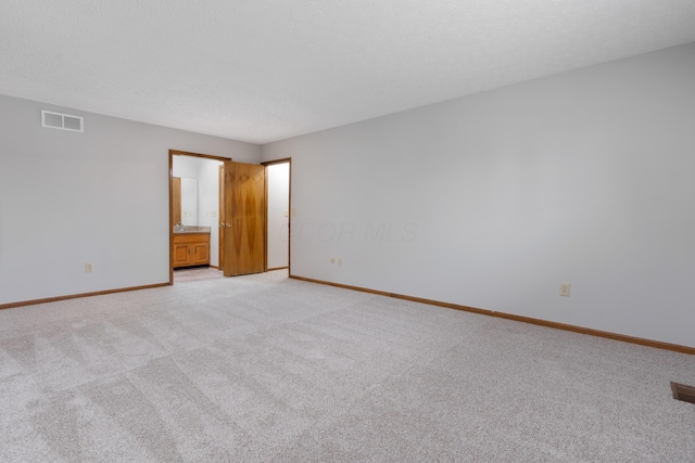 unfurnished bedroom featuring baseboards, visible vents, light colored carpet, ensuite bath, and a textured ceiling