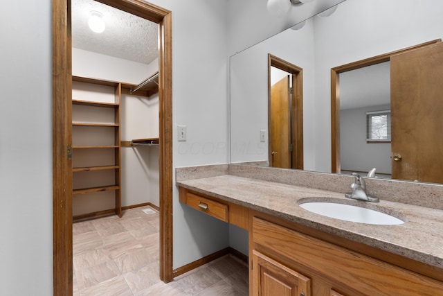 bathroom with a textured ceiling, a spacious closet, vanity, and baseboards