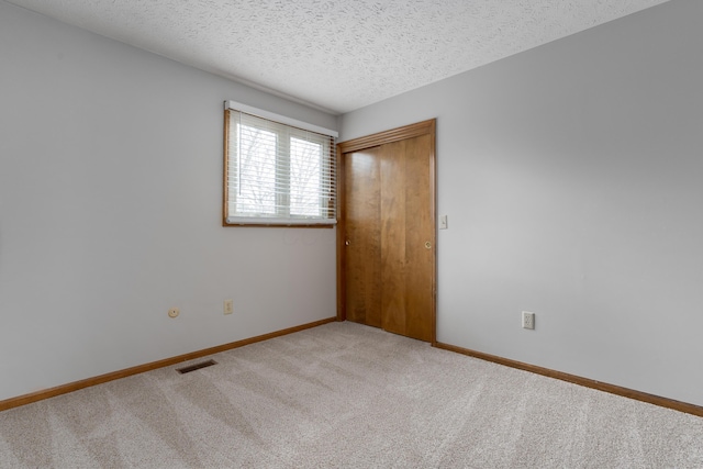 unfurnished bedroom featuring a textured ceiling, carpet floors, visible vents, baseboards, and a closet