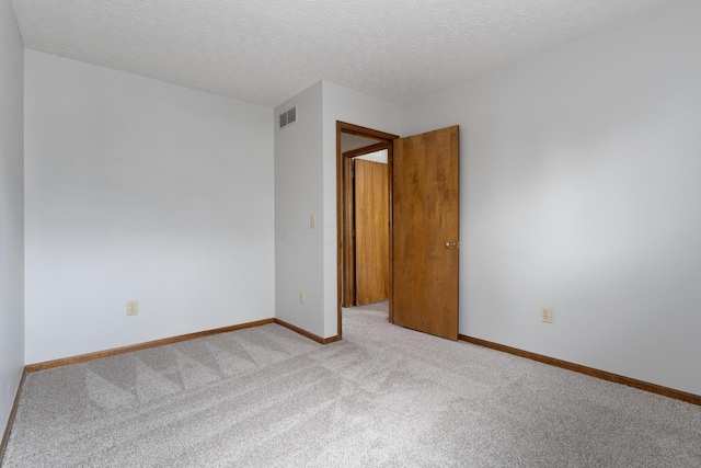 carpeted empty room featuring visible vents, a textured ceiling, and baseboards