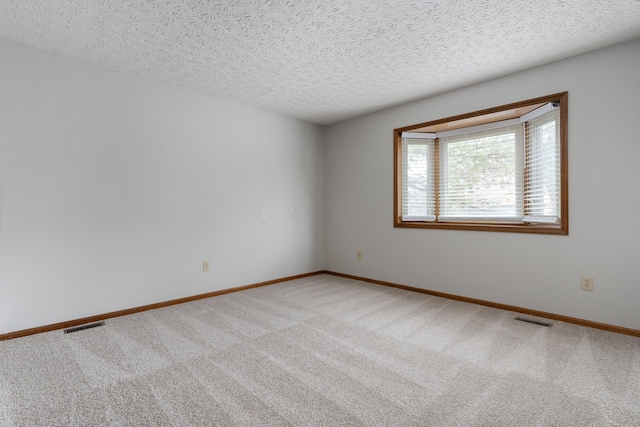 carpeted empty room featuring a textured ceiling, visible vents, and baseboards