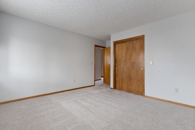 unfurnished room featuring baseboards, a textured ceiling, and light colored carpet