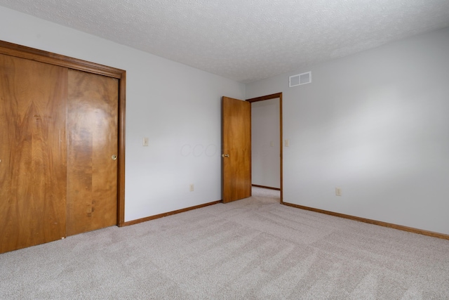 unfurnished bedroom featuring a textured ceiling, baseboards, visible vents, and light colored carpet