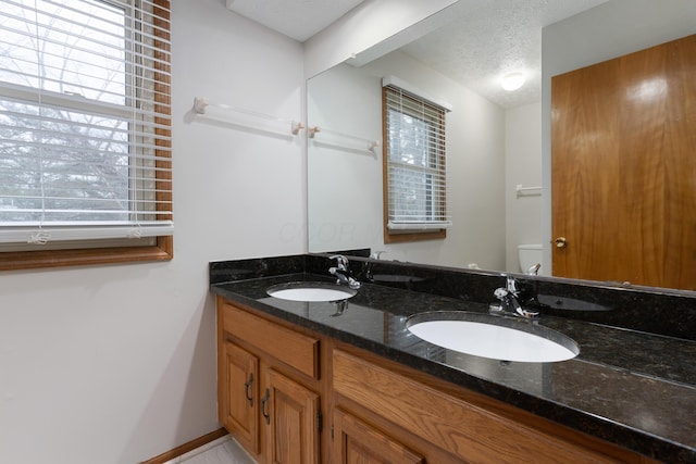 bathroom featuring a textured ceiling, double vanity, a sink, and toilet